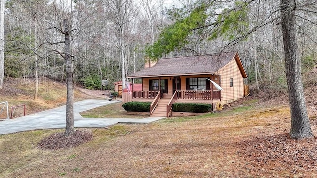 view of front facade with a porch, driveway, and a forest view