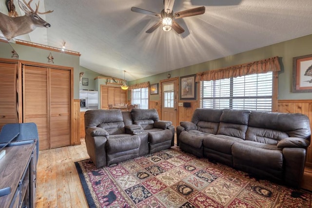 living room with lofted ceiling, a textured ceiling, wood walls, wainscoting, and light wood finished floors