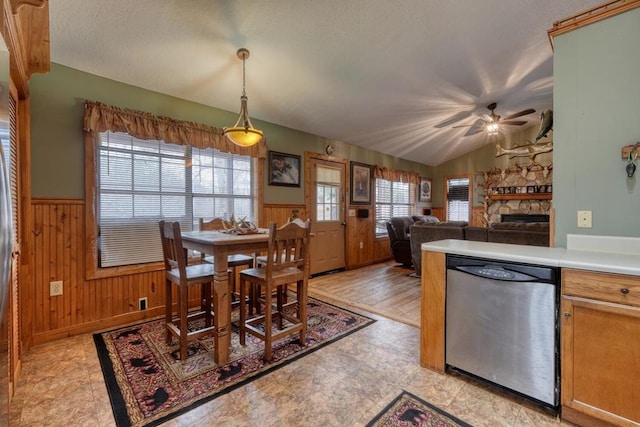 dining area featuring a wainscoted wall, wood walls, a fireplace, and lofted ceiling