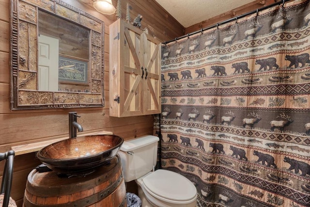 full bathroom featuring curtained shower, toilet, wood walls, vanity, and a textured ceiling