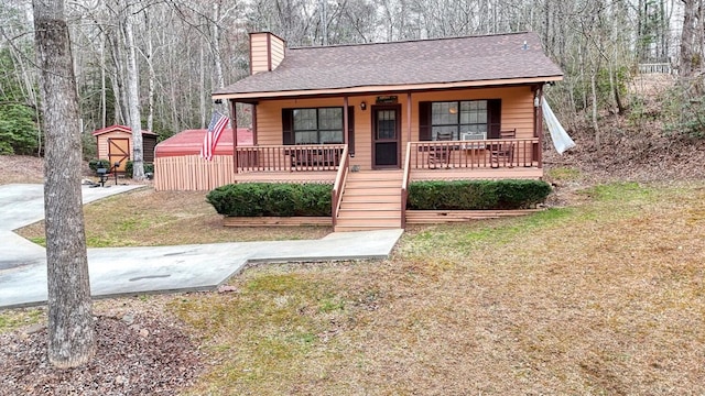 bungalow featuring a chimney, a storage unit, a porch, a front yard, and an outdoor structure