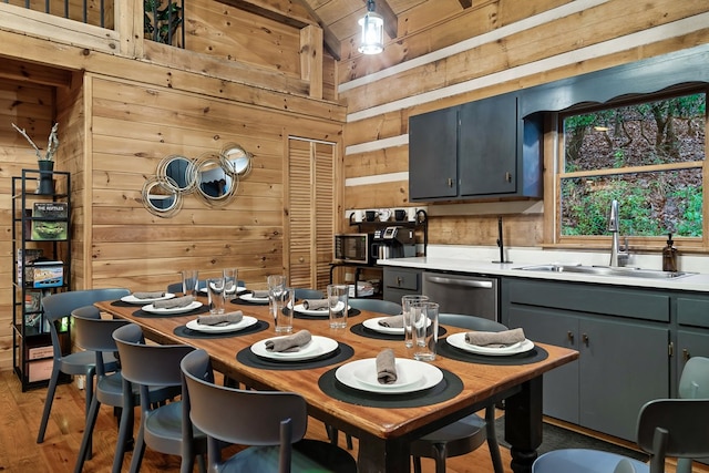 interior space with gray cabinets, light countertops, a sink, wooden walls, and dishwasher