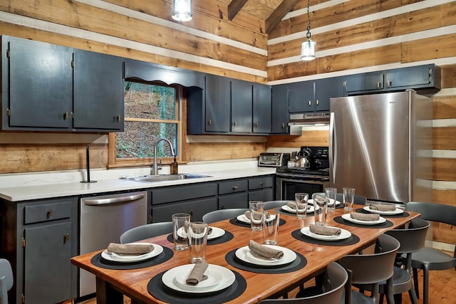 kitchen with wooden walls, appliances with stainless steel finishes, vaulted ceiling, light countertops, and under cabinet range hood