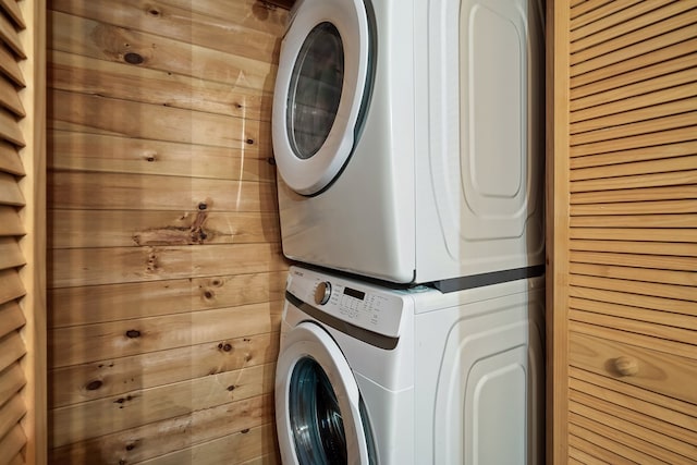 laundry area with stacked washer / dryer, laundry area, and wooden walls