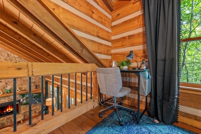 home office with lofted ceiling, a stone fireplace, wood walls, and wood finished floors