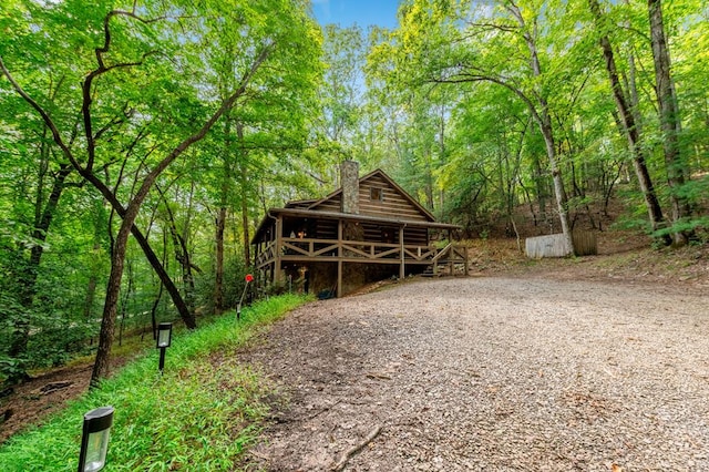 view of front of house with covered porch, a forest view, and a chimney