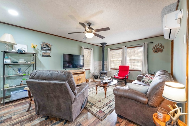 living area with a wall mounted AC, a textured ceiling, a wood stove, ceiling fan, and wood finished floors