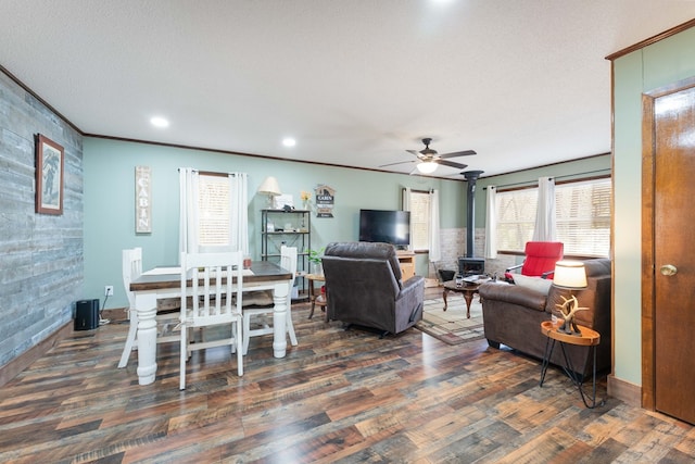 living room featuring a wood stove, ceiling fan, crown molding, and wood finished floors