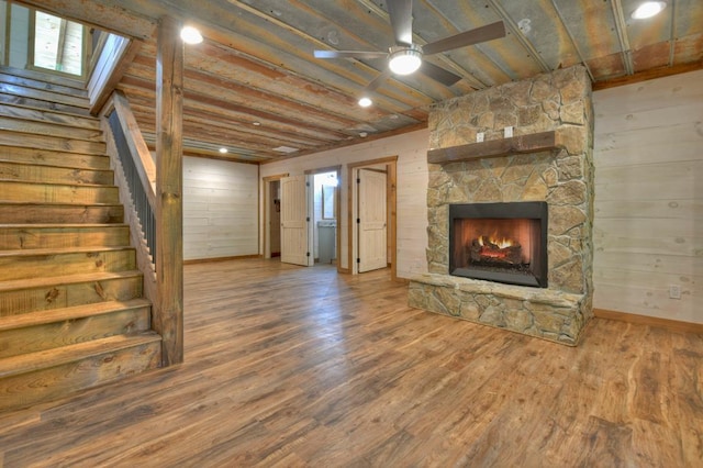 unfurnished living room with wood-type flooring, a stone fireplace, ceiling fan, and wooden walls