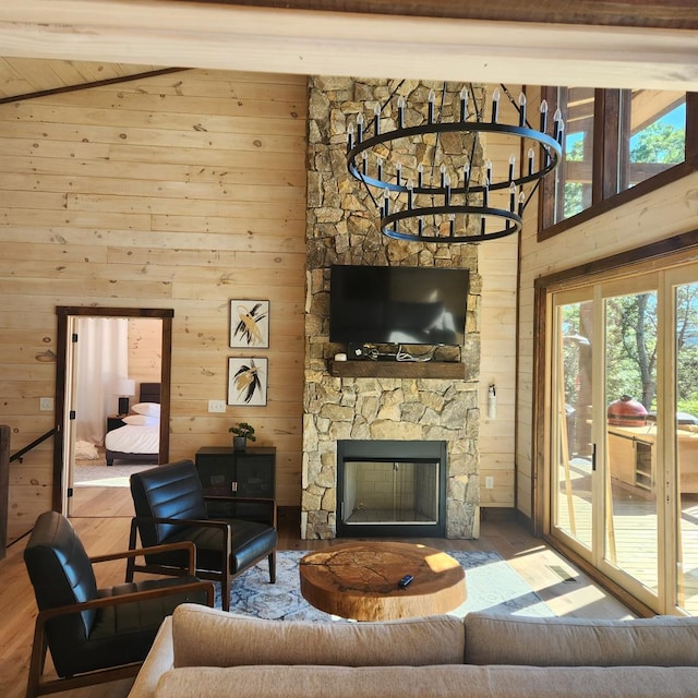 living room with an inviting chandelier, a stone fireplace, lofted ceiling with beams, wood walls, and hardwood / wood-style flooring