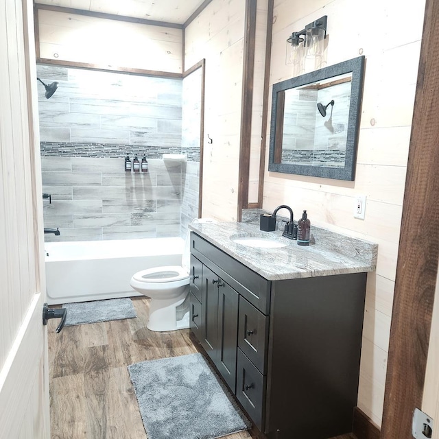 full bathroom with vanity, tiled shower / bath combo, wooden walls, hardwood / wood-style floors, and toilet