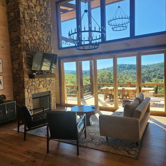 living room featuring dark hardwood / wood-style flooring, a stone fireplace, a notable chandelier, and wood walls