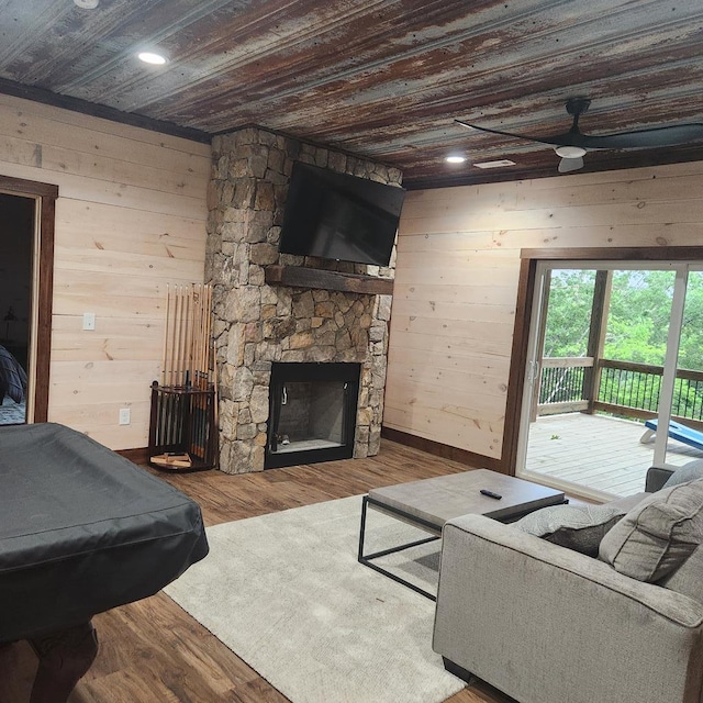 living room with wood walls, a stone fireplace, wood-type flooring, and wooden ceiling