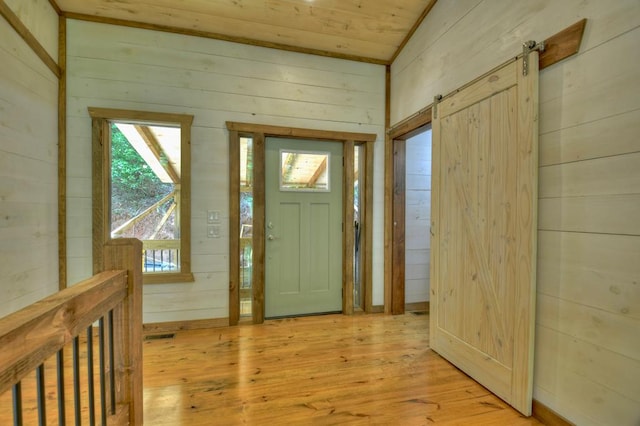 entryway featuring a barn door, light hardwood / wood-style flooring, wooden ceiling, and wood walls