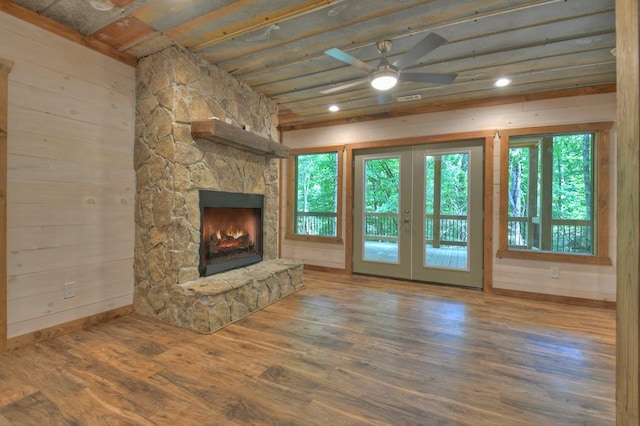 unfurnished living room featuring hardwood / wood-style floors, ceiling fan, a stone fireplace, and french doors