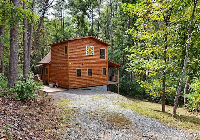 view of home's exterior featuring faux log siding, a wooded view, and gravel driveway