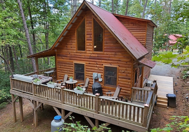 back of house with log veneer siding, a wooden deck, and metal roof