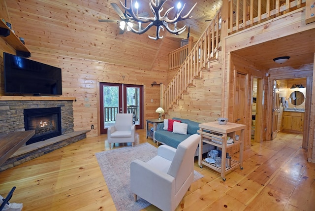 living room with stairway, wood-type flooring, wooden walls, a stone fireplace, and wooden ceiling