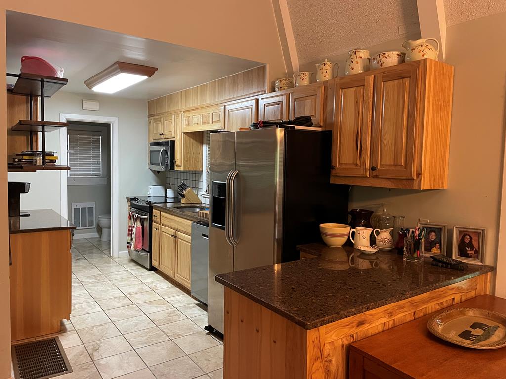 kitchen with dark stone counters, stainless steel appliances, a peninsula, tasteful backsplash, and visible vents