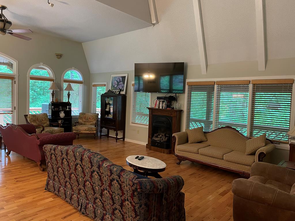 living room with a fireplace, ceiling fan, lofted ceiling with beams, and light wood finished floors