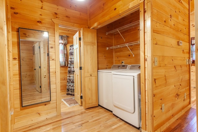 laundry area featuring washing machine and clothes dryer, light hardwood / wood-style flooring, and wooden walls