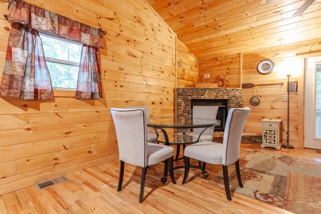 dining space featuring wooden ceiling, wooden walls, a stone fireplace, lofted ceiling, and light wood-type flooring