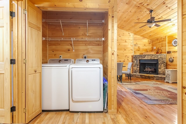 laundry area featuring light wood-type flooring, washer and dryer, a stone fireplace, wood walls, and ceiling fan