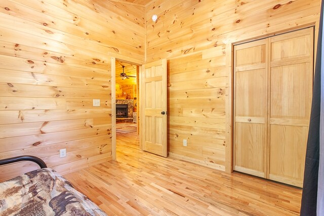 unfurnished bedroom featuring a closet, light hardwood / wood-style flooring, wood walls, and a stone fireplace