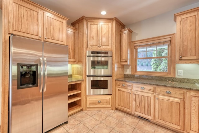 kitchen featuring light brown cabinets, stainless steel appliances, and dark stone counters