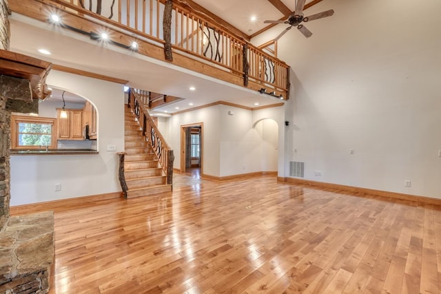 unfurnished living room with ceiling fan, light hardwood / wood-style flooring, a towering ceiling, and crown molding