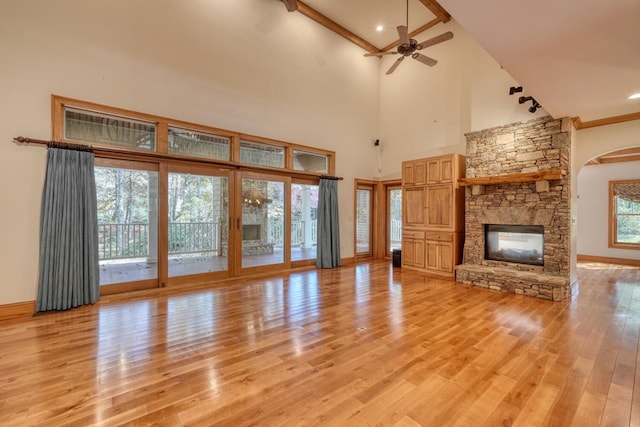 unfurnished living room with light hardwood / wood-style floors, high vaulted ceiling, ceiling fan, and a stone fireplace