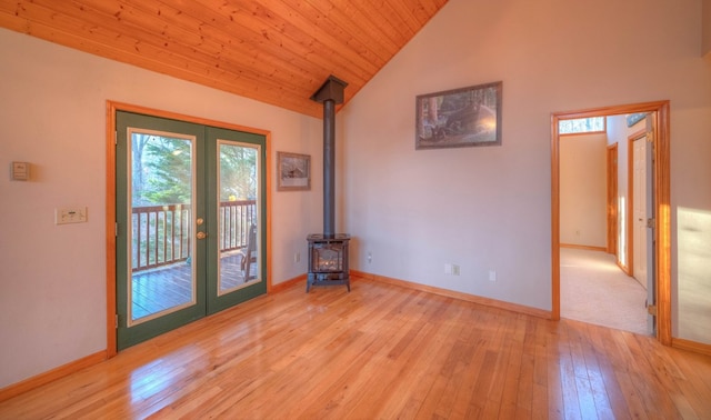 spare room with french doors, lofted ceiling, wooden ceiling, a wood stove, and light hardwood / wood-style floors