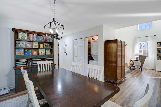 dining room featuring stacked washer / dryer, light hardwood / wood-style flooring, and a notable chandelier