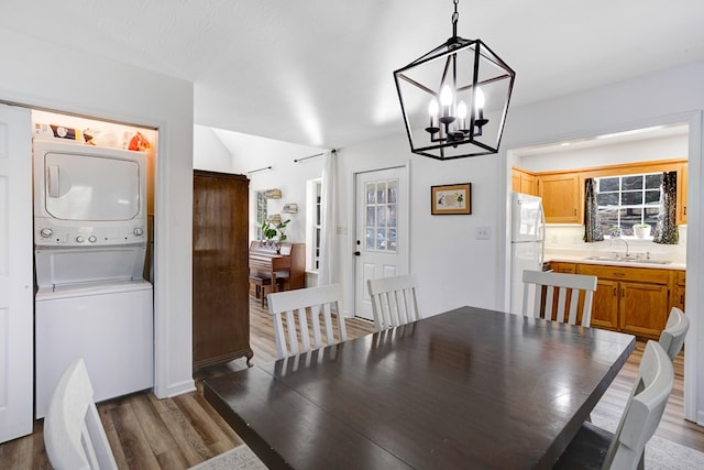 dining area featuring stacked washer and dryer, sink, a chandelier, and hardwood / wood-style flooring