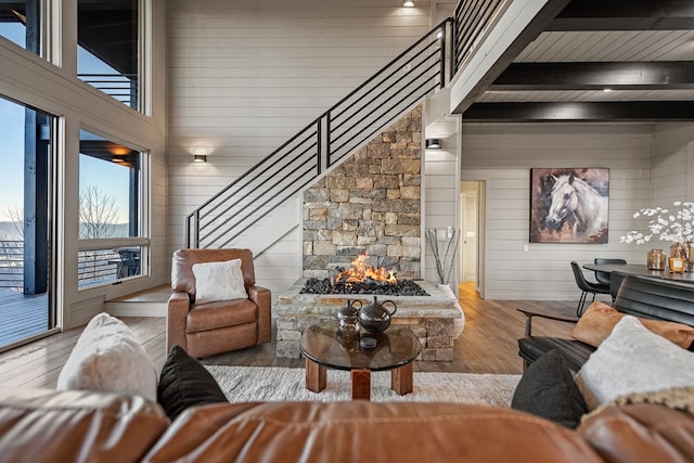 living room with beam ceiling, a towering ceiling, wooden walls, and light hardwood / wood-style flooring