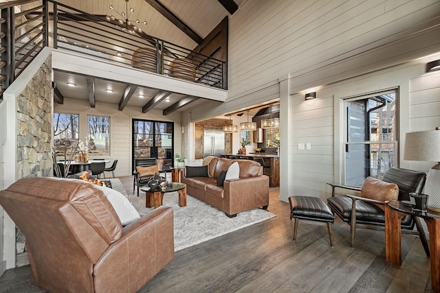 living room featuring a towering ceiling, dark hardwood / wood-style floors, beamed ceiling, a chandelier, and wood walls