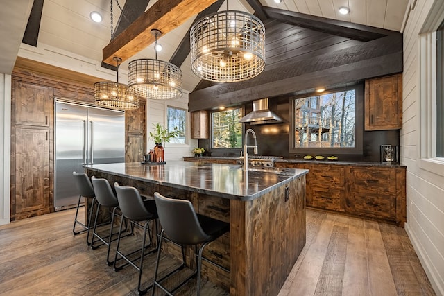 bar featuring built in fridge, pendant lighting, wood-type flooring, a notable chandelier, and wall chimney exhaust hood