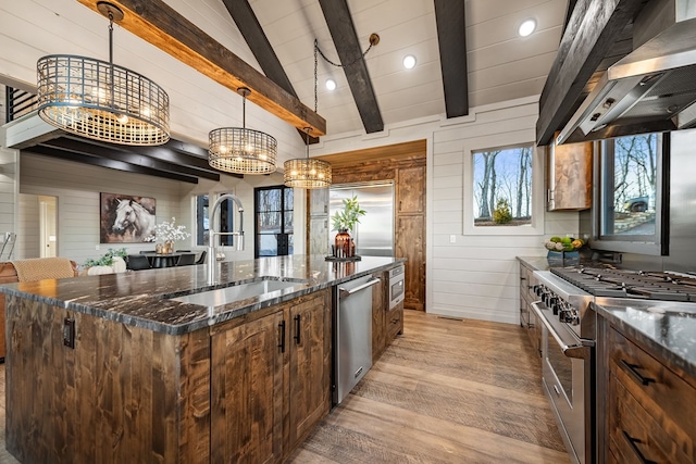 kitchen featuring appliances with stainless steel finishes, sink, dark stone countertops, hanging light fixtures, and wall chimney range hood