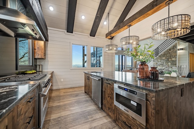 kitchen with sink, vaulted ceiling with beams, hanging light fixtures, appliances with stainless steel finishes, and wall chimney range hood