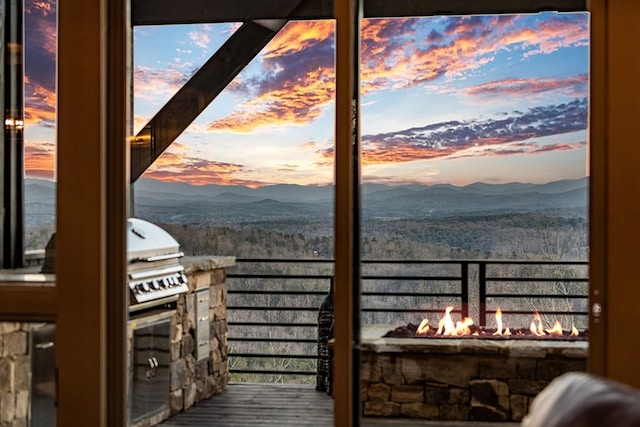 deck at dusk featuring a mountain view, area for grilling, and a fire pit