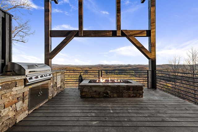 wooden deck featuring a grill, an outdoor fire pit, a mountain view, and exterior kitchen