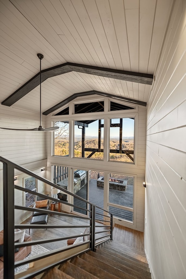 staircase with vaulted ceiling with beams, hardwood / wood-style flooring, a wealth of natural light, and wooden walls