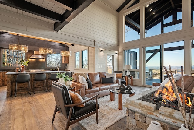 living room featuring sink, a chandelier, lofted ceiling with beams, light hardwood / wood-style flooring, and wooden walls