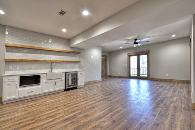 unfurnished living room featuring a sink, visible vents, wine cooler, and dark wood-style floors