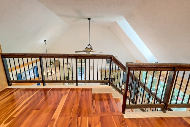 stairway with ceiling fan, vaulted ceiling with skylight, wood-type flooring, and a textured ceiling