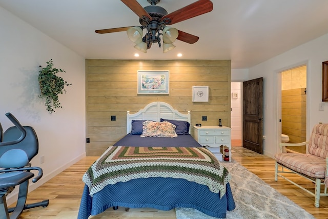 bedroom with ceiling fan, light hardwood / wood-style flooring, ensuite bathroom, and wooden walls