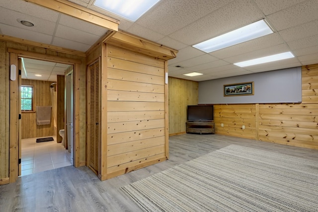 interior space featuring light wood-type flooring, a paneled ceiling, and wood walls