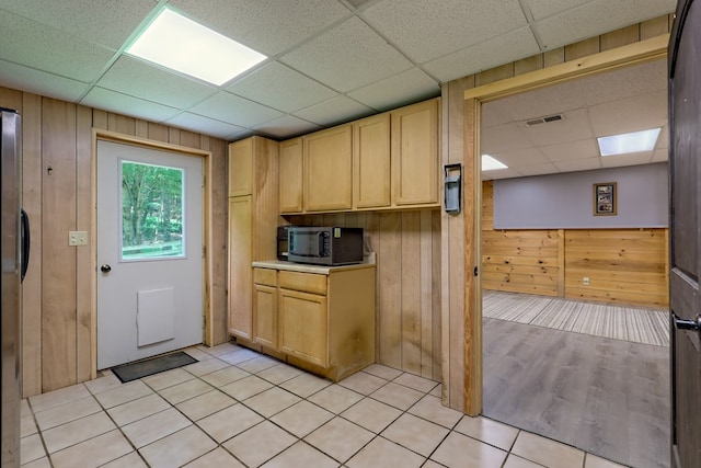 kitchen featuring a paneled ceiling, wood walls, light tile patterned floors, and appliances with stainless steel finishes