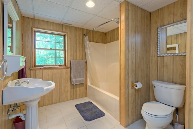 bathroom with a paneled ceiling, toilet, shower / bathtub combination with curtain, and wooden walls