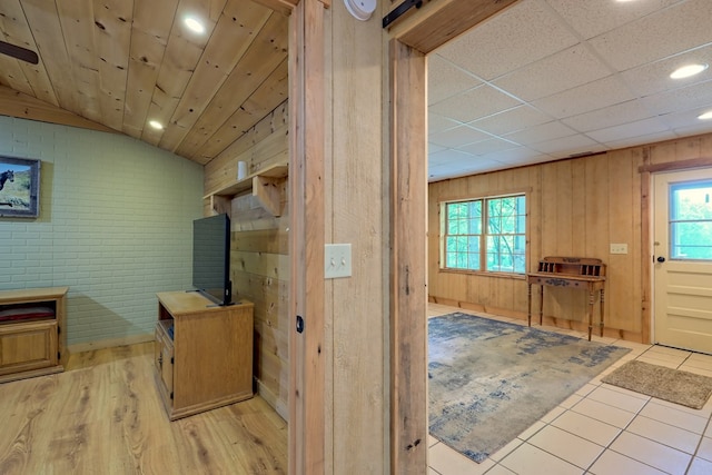 hallway featuring a barn door, brick wall, wood walls, lofted ceiling, and light tile patterned floors